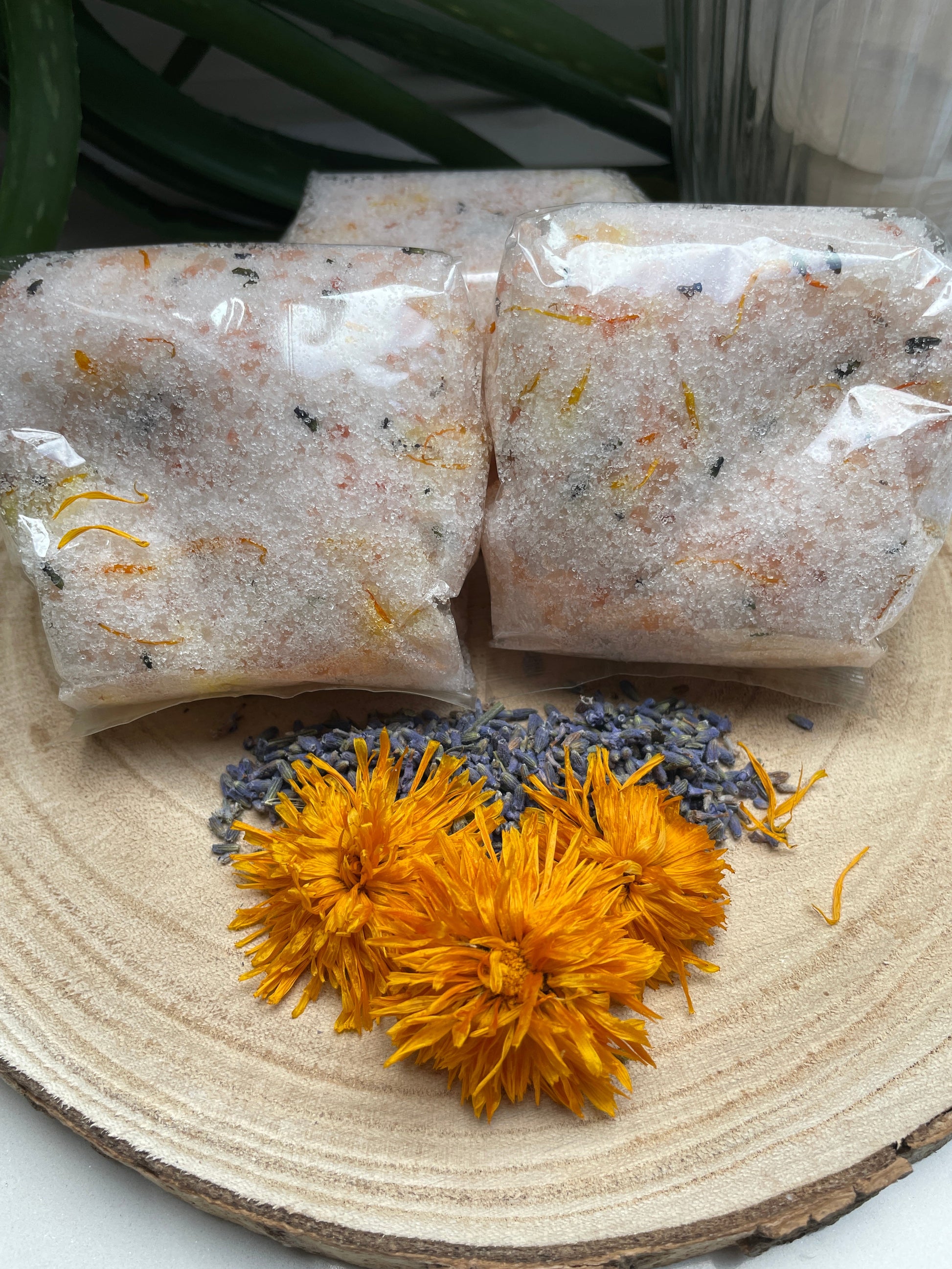 Lavender, Lemongrass & Rosemary Mineral Bath Salts completely handmade and natural, salts are in a biodegradable cellulose bag with lavender buds and calendula flowers in front.  All on a wooden board