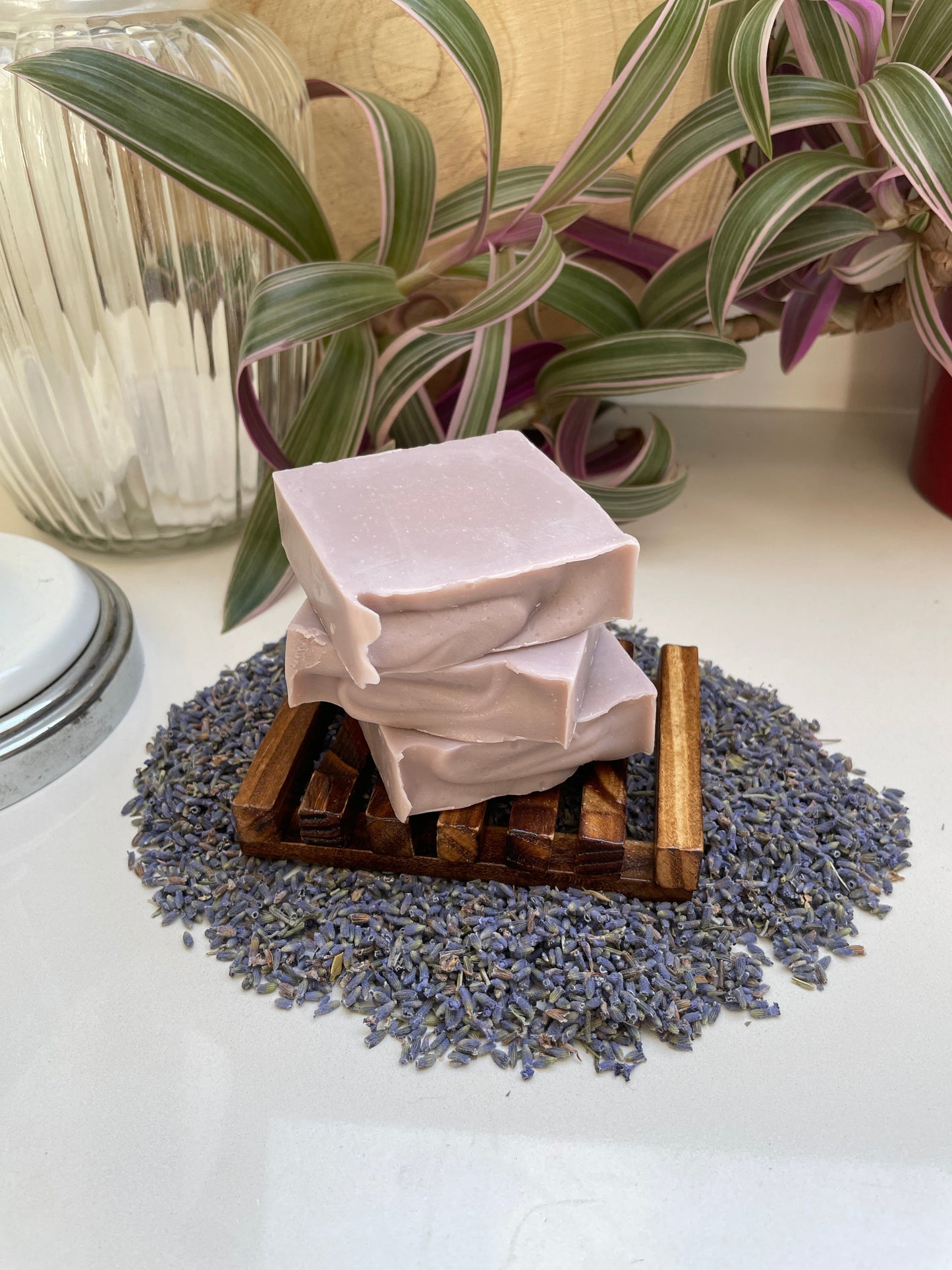 Environmentally friendly handmade lavender soap bar in a wooden soap dish resting on dried lavender.