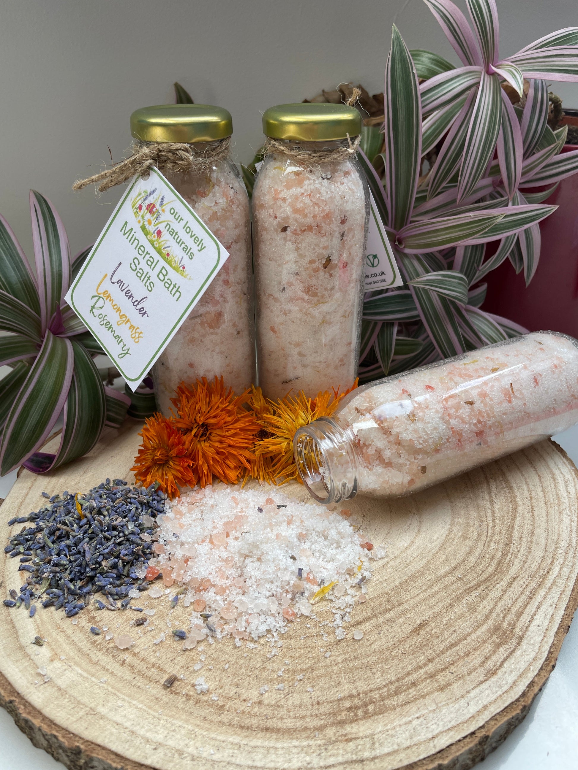 Lavender, Lemongrass & Rosemary Mineral Bath Salts completely handmade and natural, salts are in a biodegradable cellulose bag with lavender buds and calendula flowers in front.  All on a wooden board