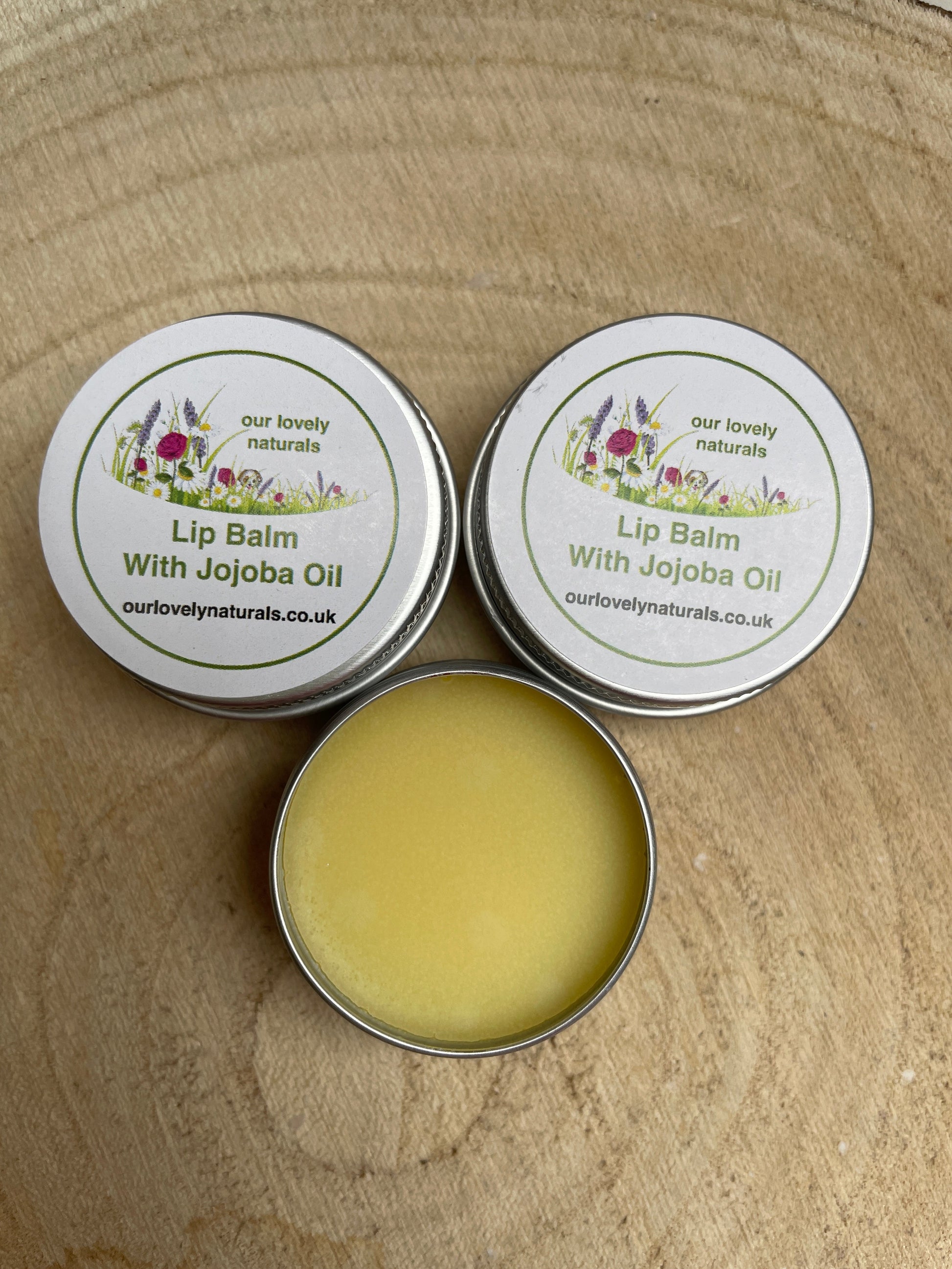 Three tins of environmentally friendly handmade lip balm with jojoba oil, one tin is open to show the contents.