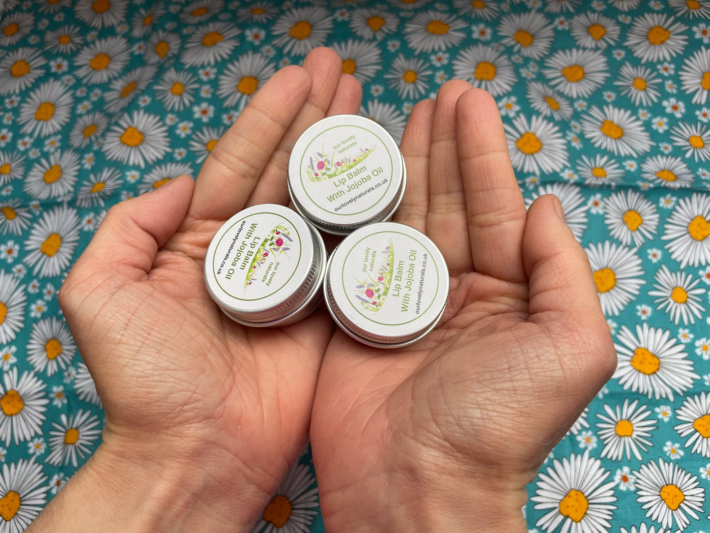 Hands holding three tins of handmade lip balm with jojoba oil.