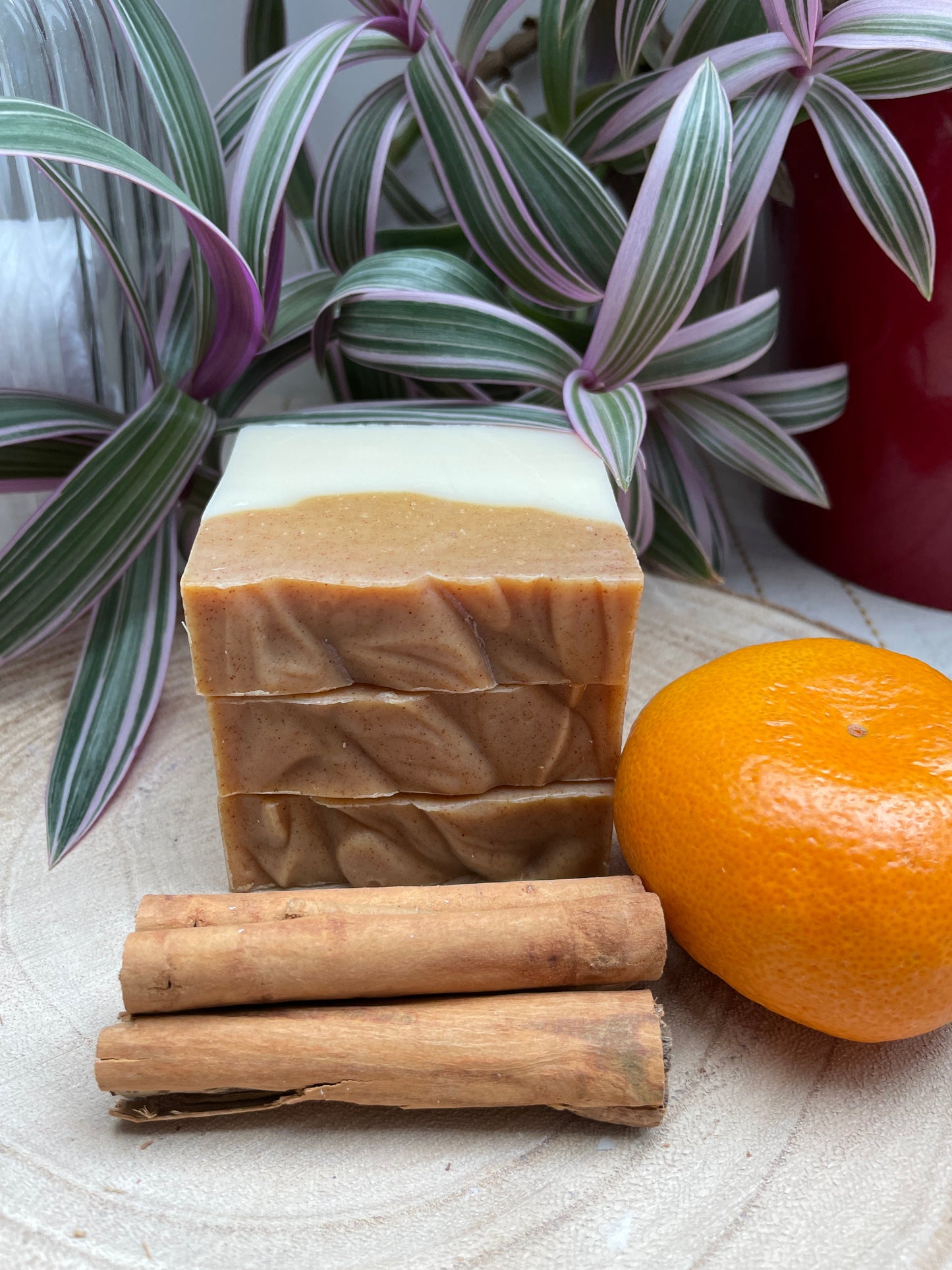 Bars of handmade environmentally friendly and natural orange & cinnamon soap bar displayed with cinnamon sticks and a small orange and plants.