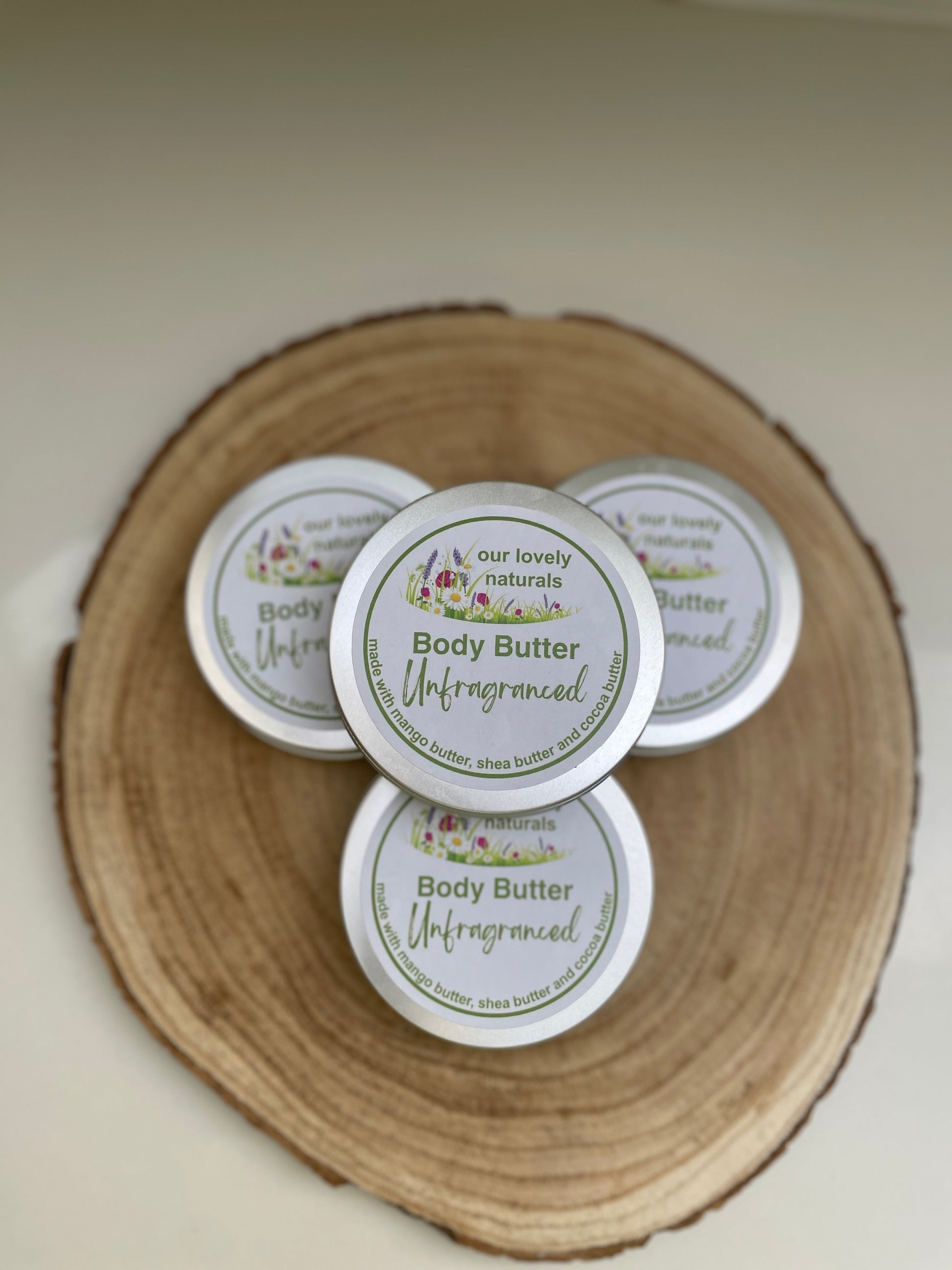 Four tins of 100% natural, handmade unfragranced body butter on a wooden board.